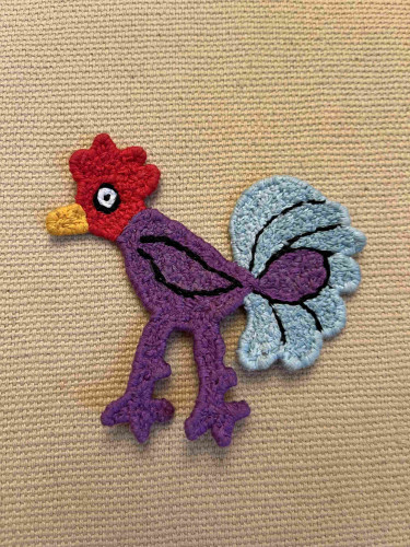 A rooster made of yarn, looking like a dense, knotted kind of flat crochet 
