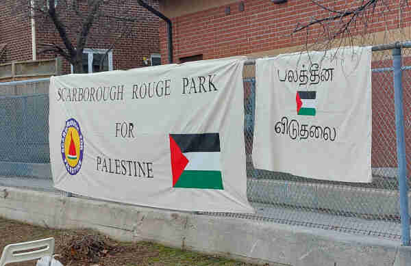 Two large banners hang on a chain mail fence.

One reads "Scarborough Rouge Park for Palestine" in English. The other is in Tamil with a small Palestinian flag.