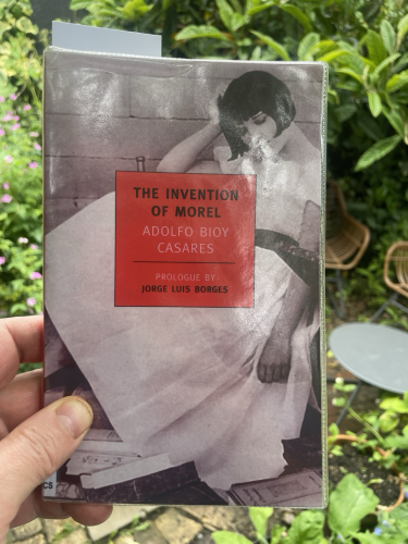 A copy of ‘The Invention of Morel’ by Adolfo Bioy Casares, in a verdant garden 