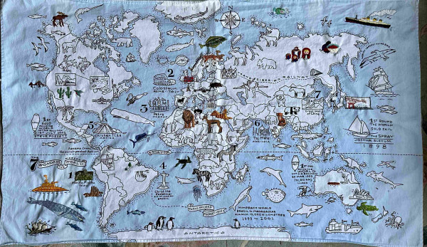 A fabric map of the world with lots of different landmarks and animals on it. Some of them have been coloured in with embroidery. 