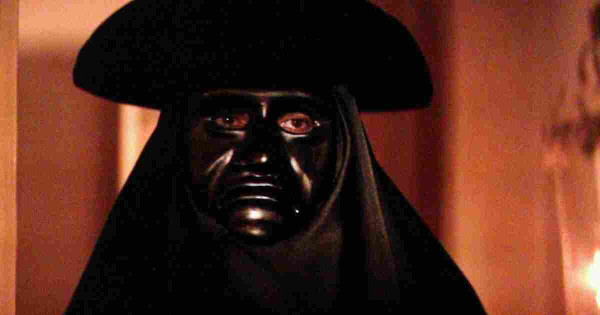 scene from the film version of "Amadeus" showing Salieri disguised in a black mask, black hood and black hat