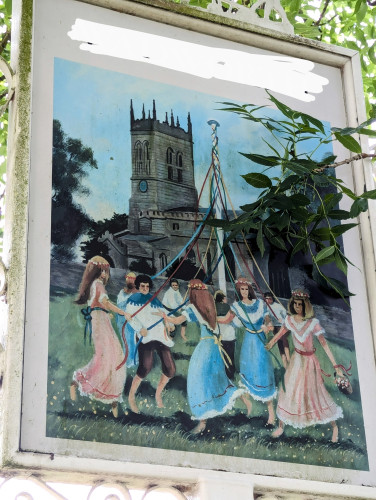 One of those "welcome to..." sign boards they put up at the entrances to English villages. This one features some country bumpkins in Merrie English Dress dancing around a maypole, with the church in the background.

Their faces are blank, expressionless, and in some cases, featureless. Their movement somehow both too much and too wooden. It is mostly girls, because heteronormativity, but one of the few guys is thrusting his hips forward like his dick has overtaken his central nervous system and is pulling him forward. It is cursed. It is haunted.

Incidentally, it is an accurate rendition of the village church.