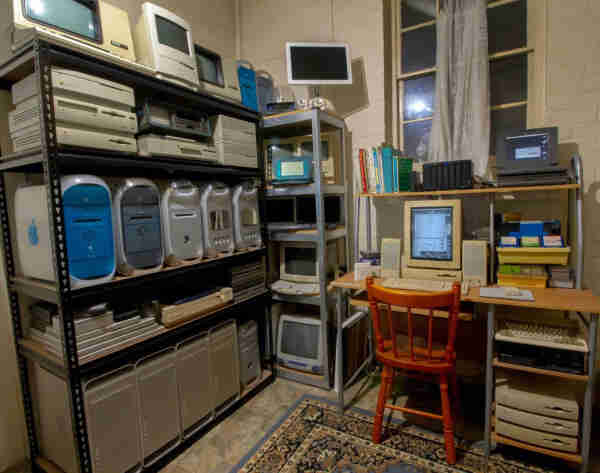 A photo of shelves of old Mac, Commodore, DEC and NeXT retro gear. The shelves stand 7ft tall and are packed with machines, while the little retro desk to the right has a Quadra 605 set up with a monochrome portrait display, speakers, floppy disks and a PowerBook. There is a modern Synology NAS looking conspicuously present, but maybe the NeXT sticker on it makes it blend in.