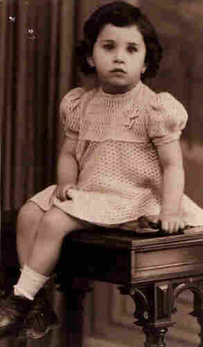 A photo of a very young girl in a dress sitting on an ornamented table. 
