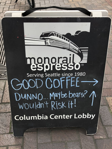 Sandwich board advertising Monorail Espresso’s Columbia Center Lobby location. It has “Serving Seattle since 1980” preprinted on it and then handwritten in chalk “Good coffee” and an arrow pointing right, followed by “Dunno…maybe bears? Wouldn’t risk it!” with an arrow pointing forward.