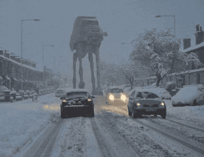 Photo of a bunch of cars driving on an ice-covered road, with a Star Wars AT-AT behind them.