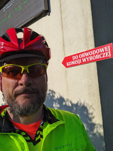 Selfie w kasku rowerowym ze znakiem wskazującym drogę do lokalu wyborczego