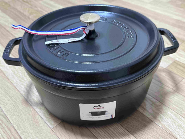 A new cast iron pot with a lid, featuring two handles and a brand label.