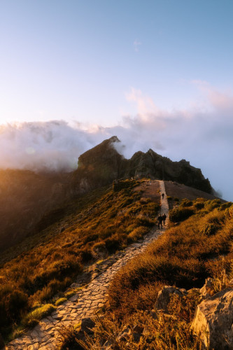 A photo of Pico do Arieiro during sunset, path leading into the mountains, clouds associated with the mountains in the background.