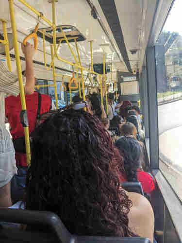 Photo showing a crowded bus, with many people standing along the corridor.