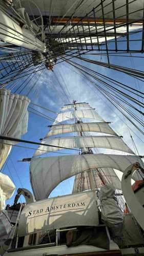 View of main mast with five of the six sails set. The stad amsterdam banner is visible on the sloop deck. 