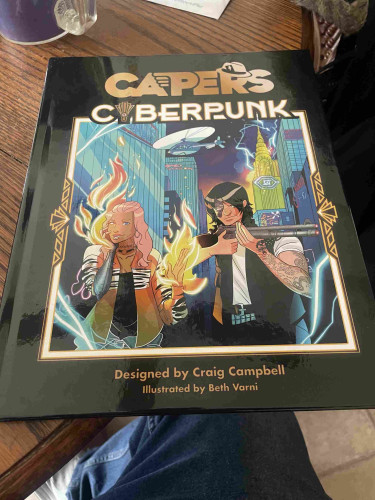 A tabletop role-playing game book titled "CAPERS Covert" with cyberpunk themed artwork, featuring stylized characters surrounded by futuristic cityscape elements. Designed by Craig Campbell and illustrated by Beth Varni.