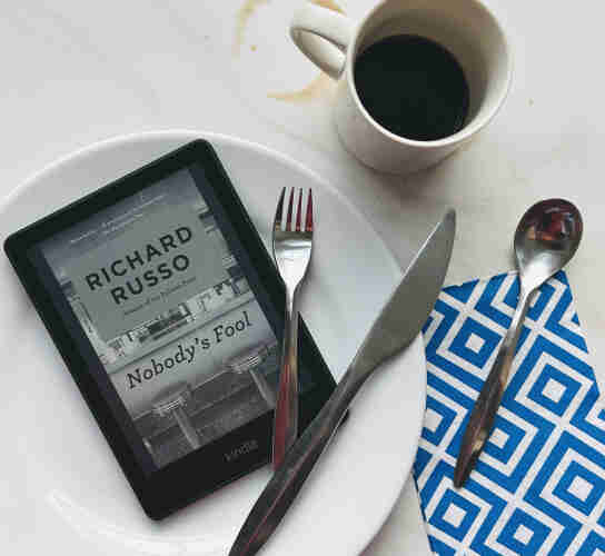 A slightly messed place setting, my Kindle with the cover of Nobody’s Fool, by Richard Russo showing (which has a diner on the cover). 