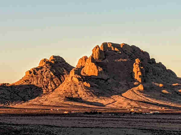 Light and shadow highlight two craggy hills which rise out of the desert floor as the setting sun casts a red glow