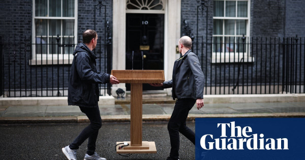 Two men carrying a wooden plinth in front of Ten Downing Street