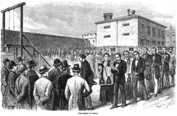 Six of the convicted Molly Maguire defendants walking to the scaffold at Pottsville, Pennsylvania from Leslie's Weekly June 21, 1877. By Frank Leslie&#039;s Illustrated Newspaper - https://books.google.com/books?id=70BaAAAAYAAJ, Public Domain, https://commons.wikimedia.org/w/index.php?curid=74205805