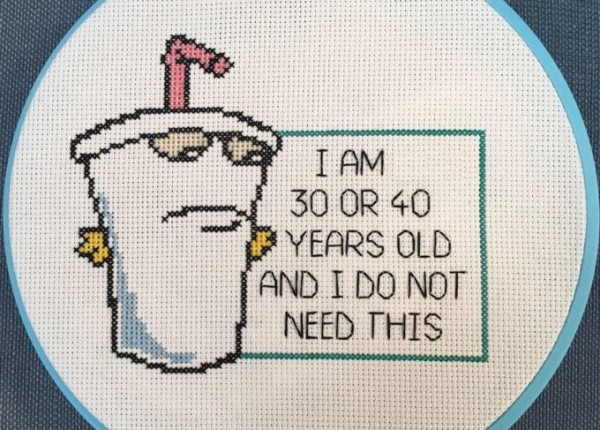 Still image. Cross stitch of Master Shake from Aqua Teen Hunger Force, a person-height animate milkshake with yellow hands and pink straw. Text reads:
I AM
30 OR 40
YEARS OLD
AND I DO NOT
NEED THIS