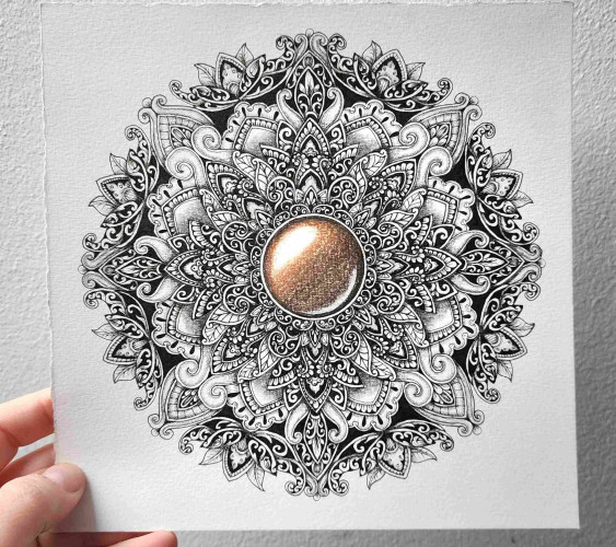 An intricate, ornate, detailed mandala hand-drawn in black ink, with a brown-coloured gemstone in the middle in coloured pencil.The mandala is shaded giving all the leaves and patterns a 3D look. In this photo, my hand is visible holding up the paper against a white wall.