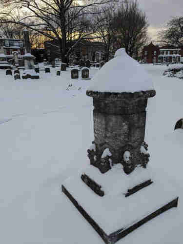 Multi-faceted marble monument in a Victorian era cemetery.  Darkened with age, covered in snow. 6 faces of the monument have children's names and dates of birth and death. 