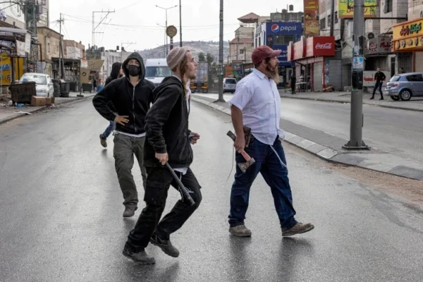 Israeli settlers walk with batons and axes along a street in the town of Huwara in the occupied West Bank on October 13, 2022 [Oren Ziv/AFP]
