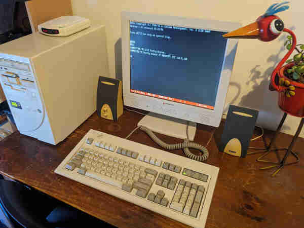An old 486 in a tower case with a modem on top of it, a Model M keyboard and an LCD monitor showing a Telix session.