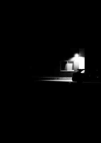 A lonely car parked in a parking lot, under a lamp.