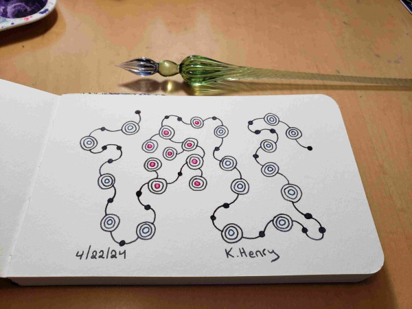 Hand drawn generative art in ink on an open page of my new sketchbook. The abstract pattern is kinda like beads on a string. My glass dipping pen is next to my sketchbook.