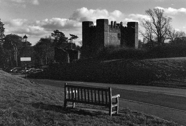 Black and white photo showing a wooden bench across the road from Castle buildings. The photo is very low key and shows massive grain, whether under-exposed or wrongly-developed, I don't know. Taken with Pentax MX using the SMC M 50/1.7 lens on XP2 developed in HC-110 at home.