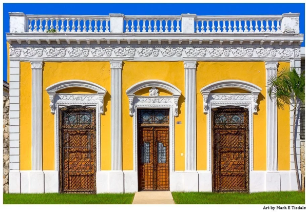 Ornate architecture - symmetrical row of one door flanked by two windows with ornate plasterwork columns and decoration. The architecture is bright yellow with white trim with a hint of blue sky overhead..
