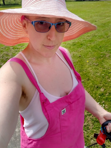 Alexis wearing bright pink dungarees with a pale pink strappy top under them and a large pale pink and white sun hat.