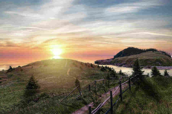The sun rises colourfully over a section of the East Coast Trail near Tors Cove, Newfoundland, bathing the Atlantic Ocean and surrounding landscape in soft light. 