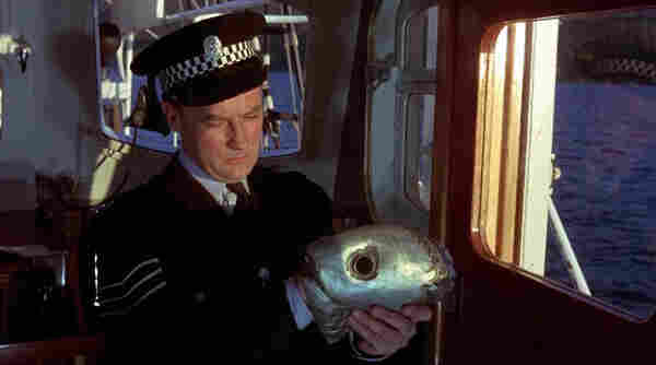 A police officer on a seaplane quizzically looks at a fish mask