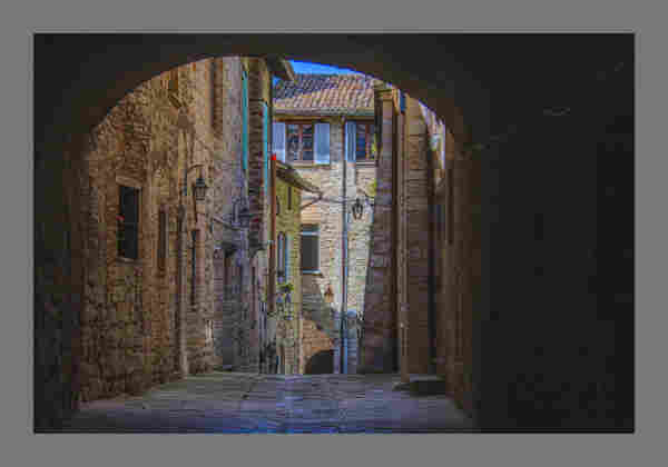 Stone houses line a narrow street seen through a dark arch
