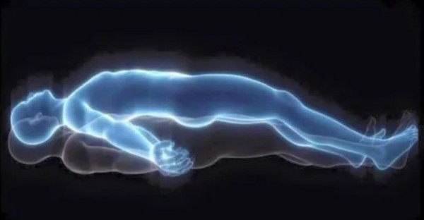 A glowing, translucent human figure lying horizontally, with its outline highlighted in a bluish hue, suggesting an ethereal or spiritual form. The figure appears to be floating just above another solid body, giving the impression of an out-of-body experience or astral projection. The background is dark, enhancing the glowing effect of the figure.
