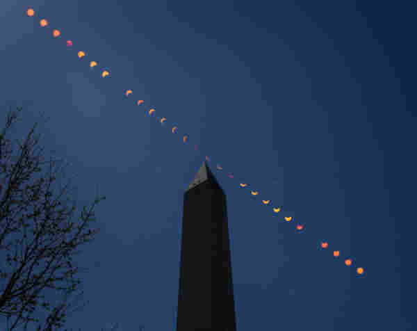 This composite image shows the progression of a partial solar eclipse over the Washington Monument in Washington. The orange Sun and lunar shadow track from the upper left to the lower right of the frame, across a dark blue sky over the pointed tip of the silhouetted obelisk. The bare branches of a tree reach into the lower left side of the frame. Credit: NASA/Bill Ingalls⁣