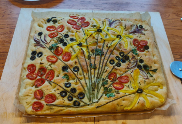 A Focaccia decorated with tomatoes, paprika, olives, chives, etc. in the form of a flower painting.