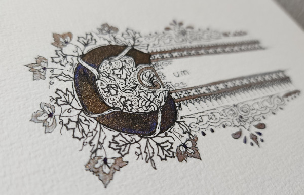 Angled view of blue-bronze shimmery ink inside an ornate letter 'C' surrounded by vines and flowers, then the letters 'um' written simply in black ink to the side, spelling 'cum', with an ornate decorative border at the top and bottom. 