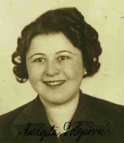 An ID portrait photo of a woman. She has dark curly hair and wide smile that exposes her teeth. She has a round face and thin eye-brows. You can see her hand-written signature in the photo.