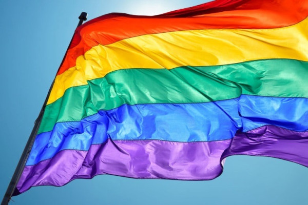 Rainbow pride flag fluttering against a blue sky.