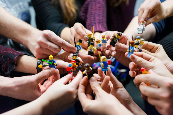 A photo of a group of hands holding lego minifigs. 