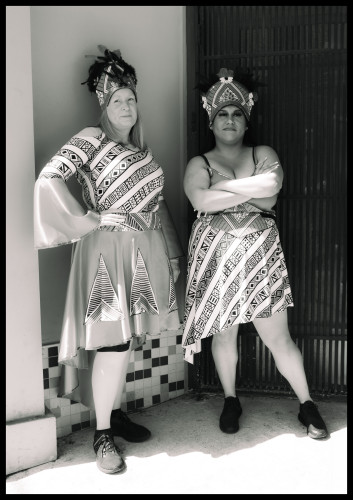 Two women in festive dresses stand in the shade of a building entryway, awaiting the start of the Annual Carnaval parade in The Mission. One with arms on her hip, the other with arms crossed in front... the give me "the look" of slight impatience but tolerance as I snap the photo.

Monochrome. 