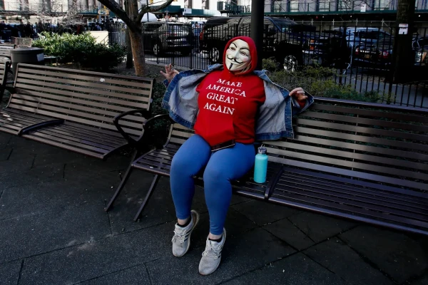 Single, lone Trump supporter sitting on a bench near the NYC courthouse wearing a QAnon mask and a red Trump sweatshirt labeled, "Make America Great Again"