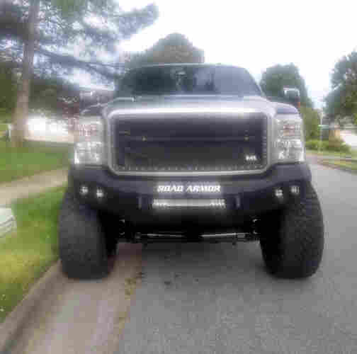 Photo I took of a giant pickup truck parked on the street in my neighborhood. It has oversize tires, a massive grill, and a bumper with the label "road armor".