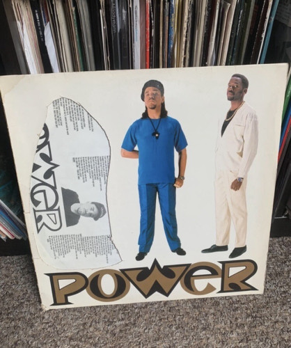 Album cover of "Power" featuring two men standing side by side, with a collection of records visible in the background. Next to the two men on the cover, there is a hole cut out of about the size of a third human figure.
