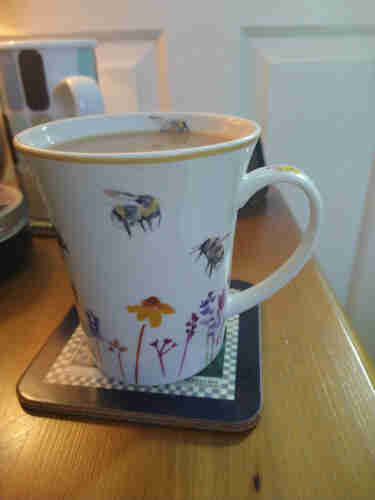 Mug of tea on a bedside cabinet with flowers and bees