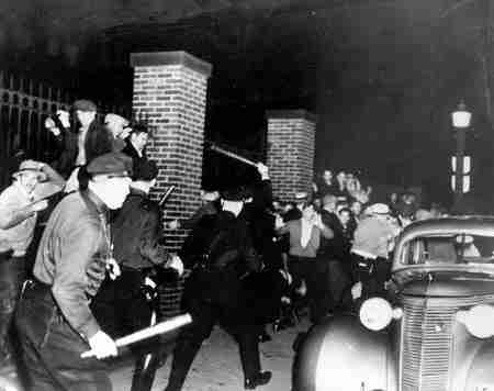 Black and white photo of police, with batons raised over their heads, attacking striking rubber workers in Akron, Ohio, 1936.