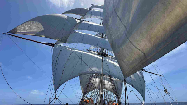 Square rigged ship with five sails on the fore mast and two large stun sails to the starboard side. 