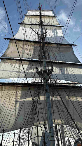 Six square sails set on the main mast with the shadows of someone standing on the foremast and its five sails  