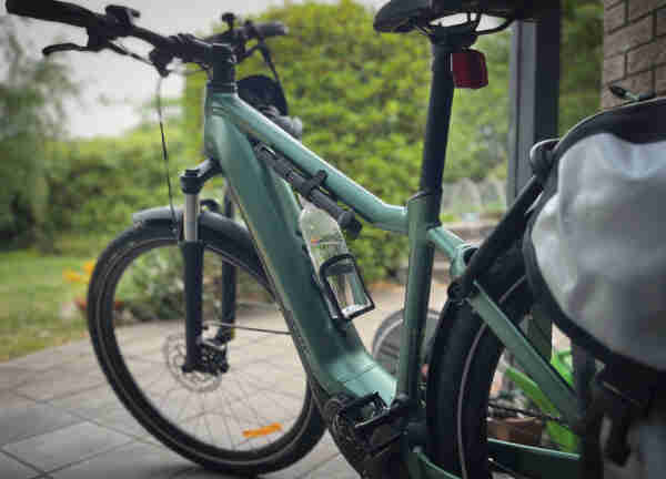 Close-up of a teal electric bicycle with a water bottle mounted on the frame, parked outdoors.