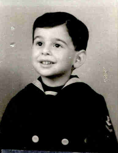 Photo of a young boy in navy clothing. He has dark hair and eyes. He looks up - his head is slightly raised.
